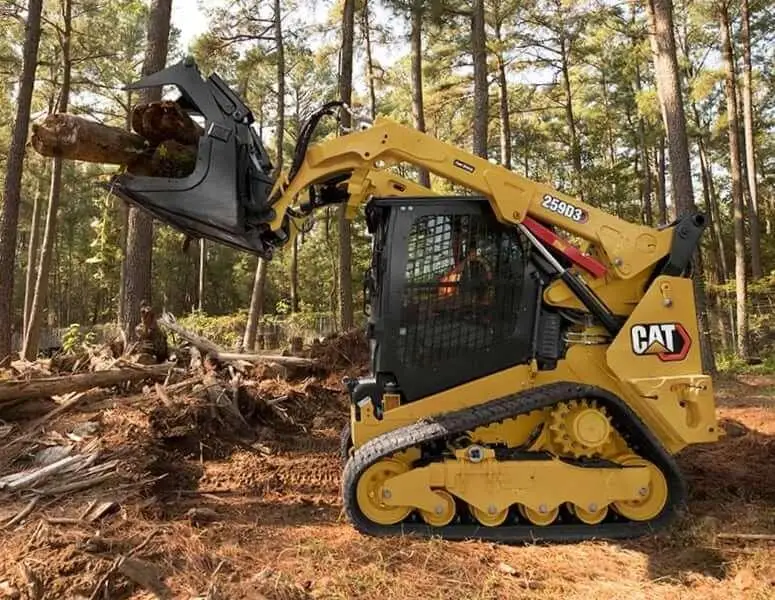 Skid steer with a grapple attachment clearing a felled tree on a wooded lot