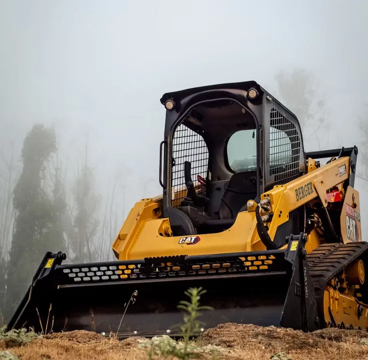 CAT skid steer with a brush attachment on a cleared hilltop lot