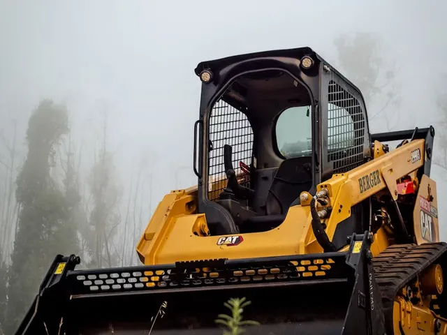 CAT skid steer with a brush attachment on a cleared hilltop lot